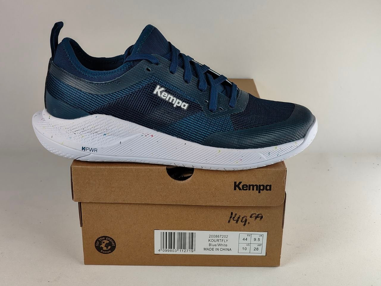 A navy blue and white Kempa athletic shoe resting on top of its brown cardboard shoebox against a plain off-white background.