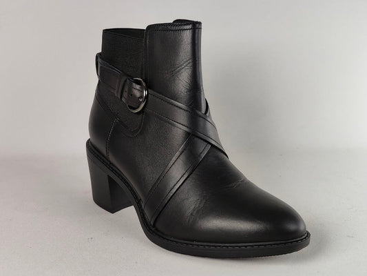 A black leather ankle boot with a block heel, featuring diagonal straps across the instep and a side buckle detail, shown against a neutral light gray background.