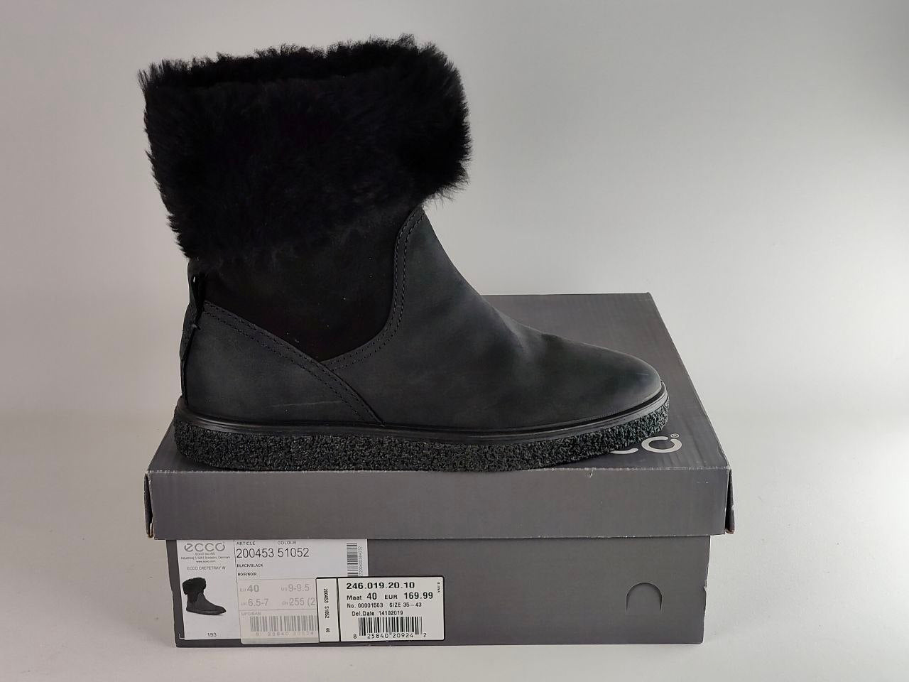 A black suede ankle boot with a fluffy black faux-fur trim, displayed on top of its dark gray ECCO shoebox against a neutral gray background.