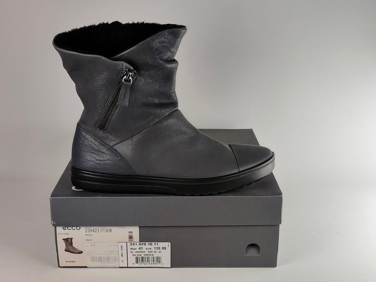 A dark gray leather ankle boot with a side zipper and black sole, displayed on top of its gray shoebox against a neutral gray background.