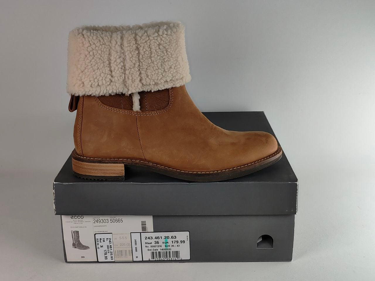 A tan suede ankle boot with a thick cream sherpa fleece cuff, displayed on top of its dark gray shoebox against a neutral gray background.