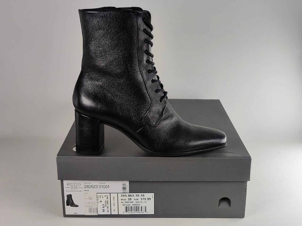 A black leather ankle boot with a block heel and laces, displayed on top of a dark gray Gucci shoebox against a neutral gray background.