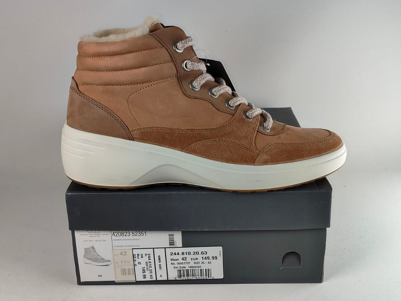 A brown suede high-top sneaker boot with a white platform sole, displayed on top of its dark gray shoebox against a neutral gray background.