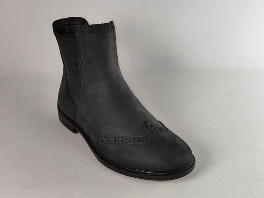 A single black leather Chelsea boot with decorative brogue perforations on the toe and side, featuring a black elastic side panel, photographed on a light gray studio background.