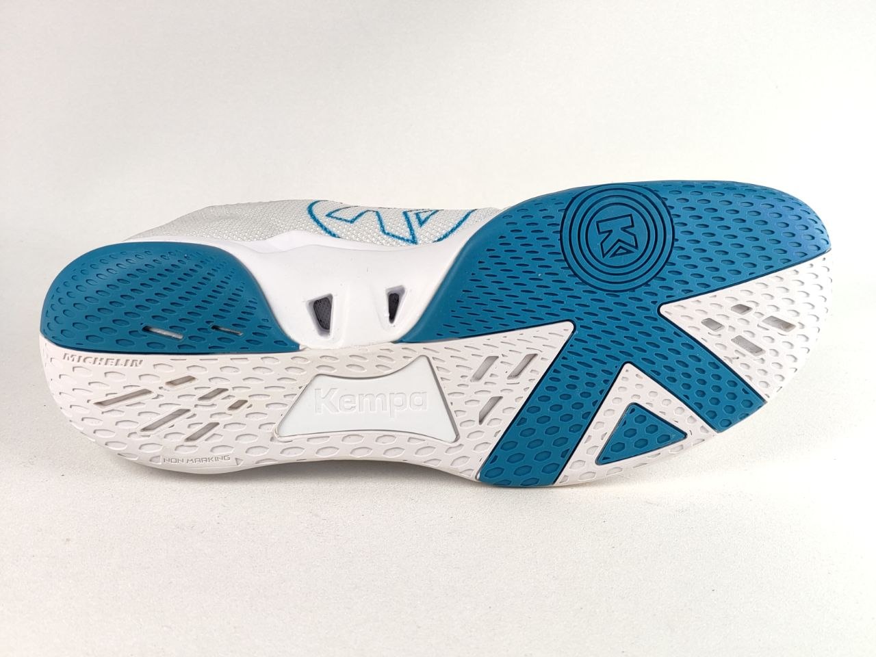 The outsole of a white and teal running shoe, showing the textured blue grip pattern and the embossed brand name 'Kempa' on the white midsole.