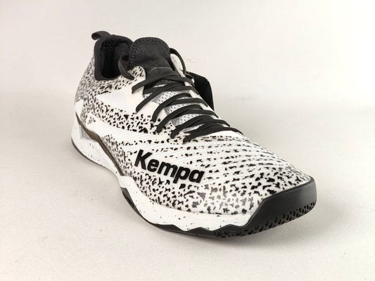 A single Kempa athletic sneaker shown from a three-quarters angle on a light gray background. The shoe features a white and black speckled knit upper, black laces, a black midsole, and a black outsole.