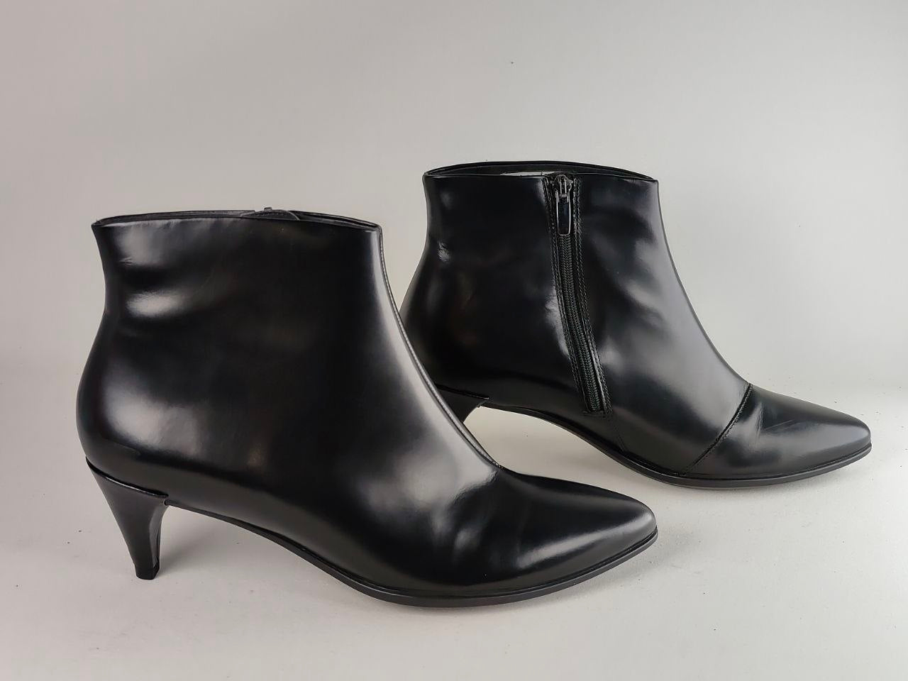 A pair of black leather ankle boots with pointed toes and kitten heels, displayed on a light gray background.