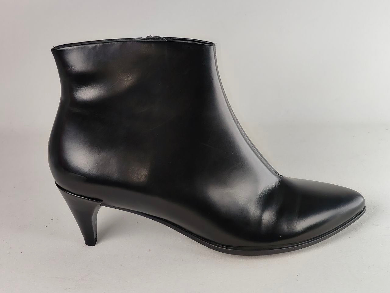 A single black leather ankle boot with a pointed toe and a low kitten heel, photographed from the side against a neutral light gray background.