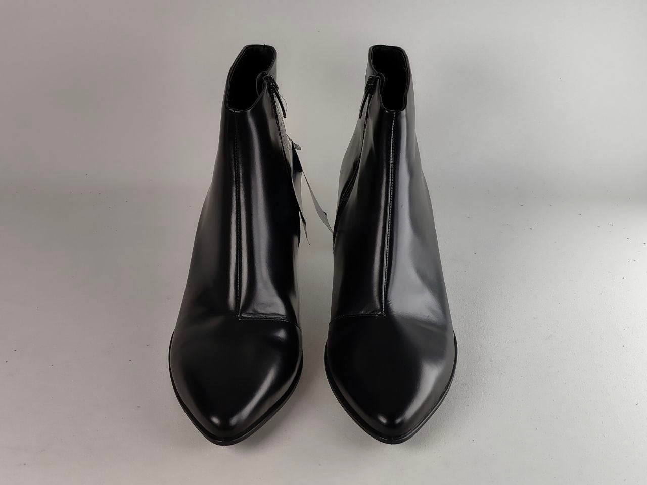 A pair of black leather ankle boots with pointed toes and side zippers, photographed against a neutral light gray background.