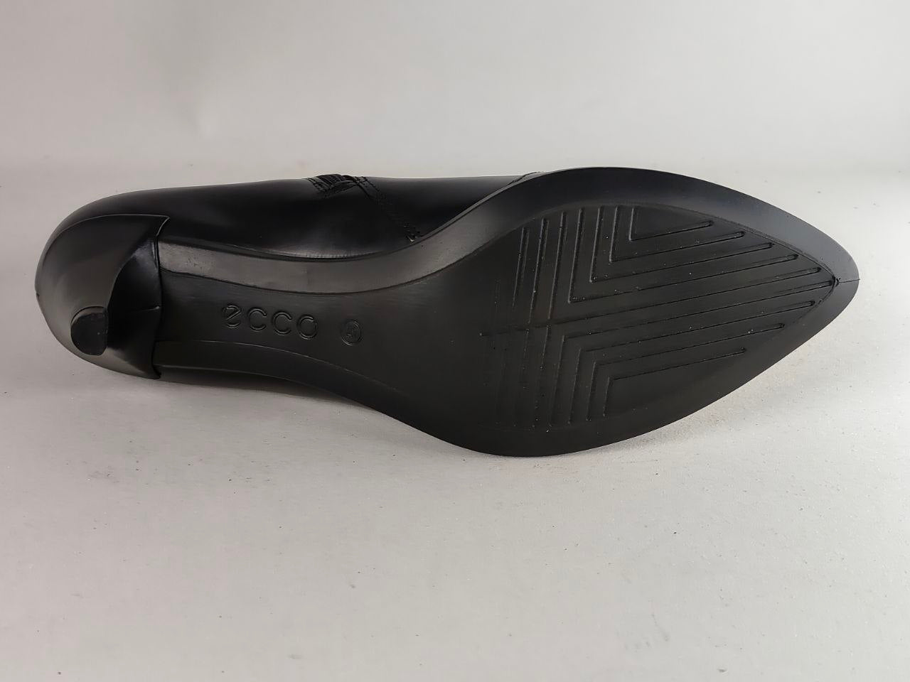 The black rubber outsole of a pointed-toe dress shoe, showing the 'ecco' brand name embossed on the heel area, photographed against a plain light gray background.