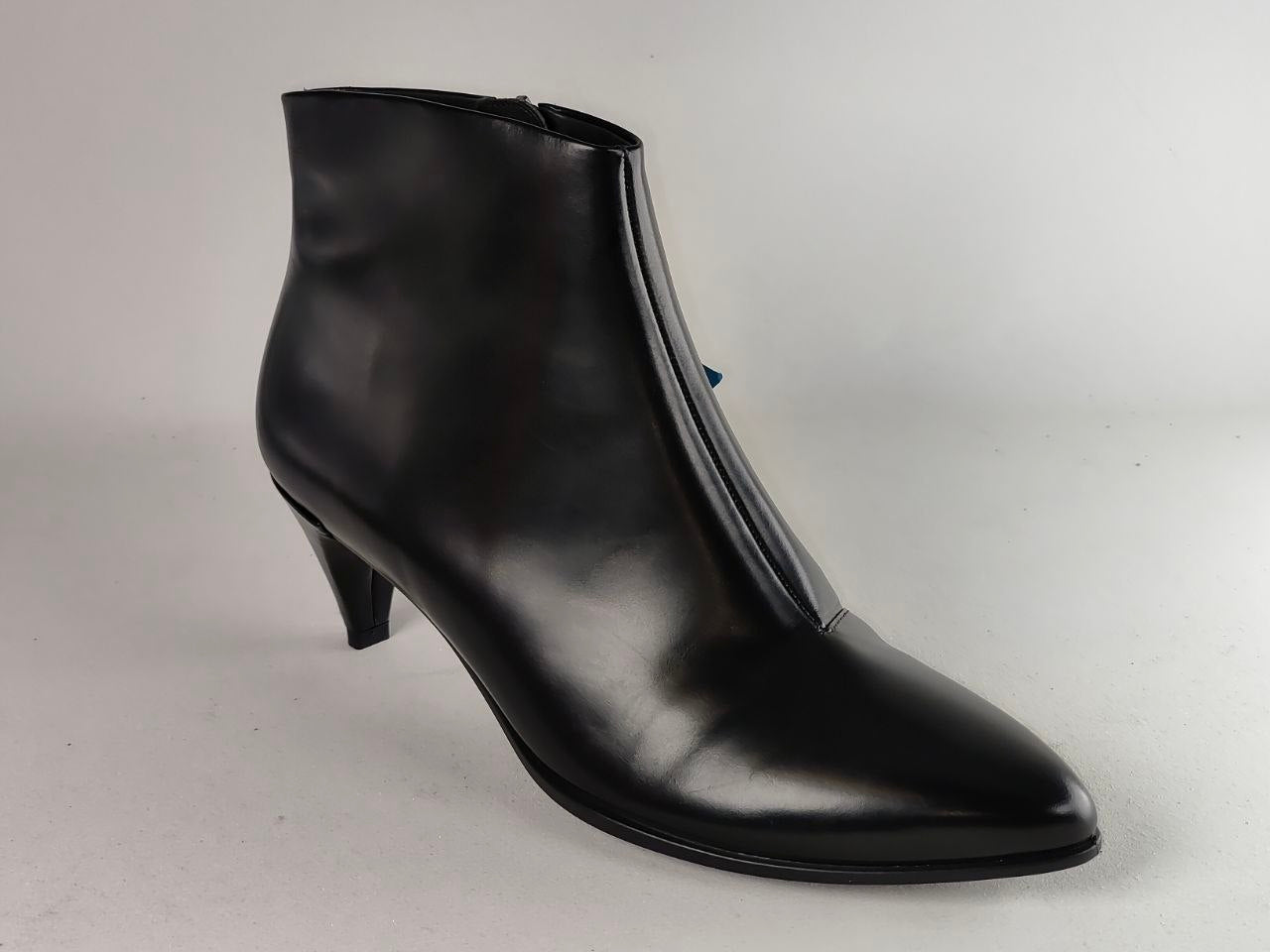 A black leather ankle boot with a pointed toe and a slim kitten heel, photographed against a neutral light gray background.