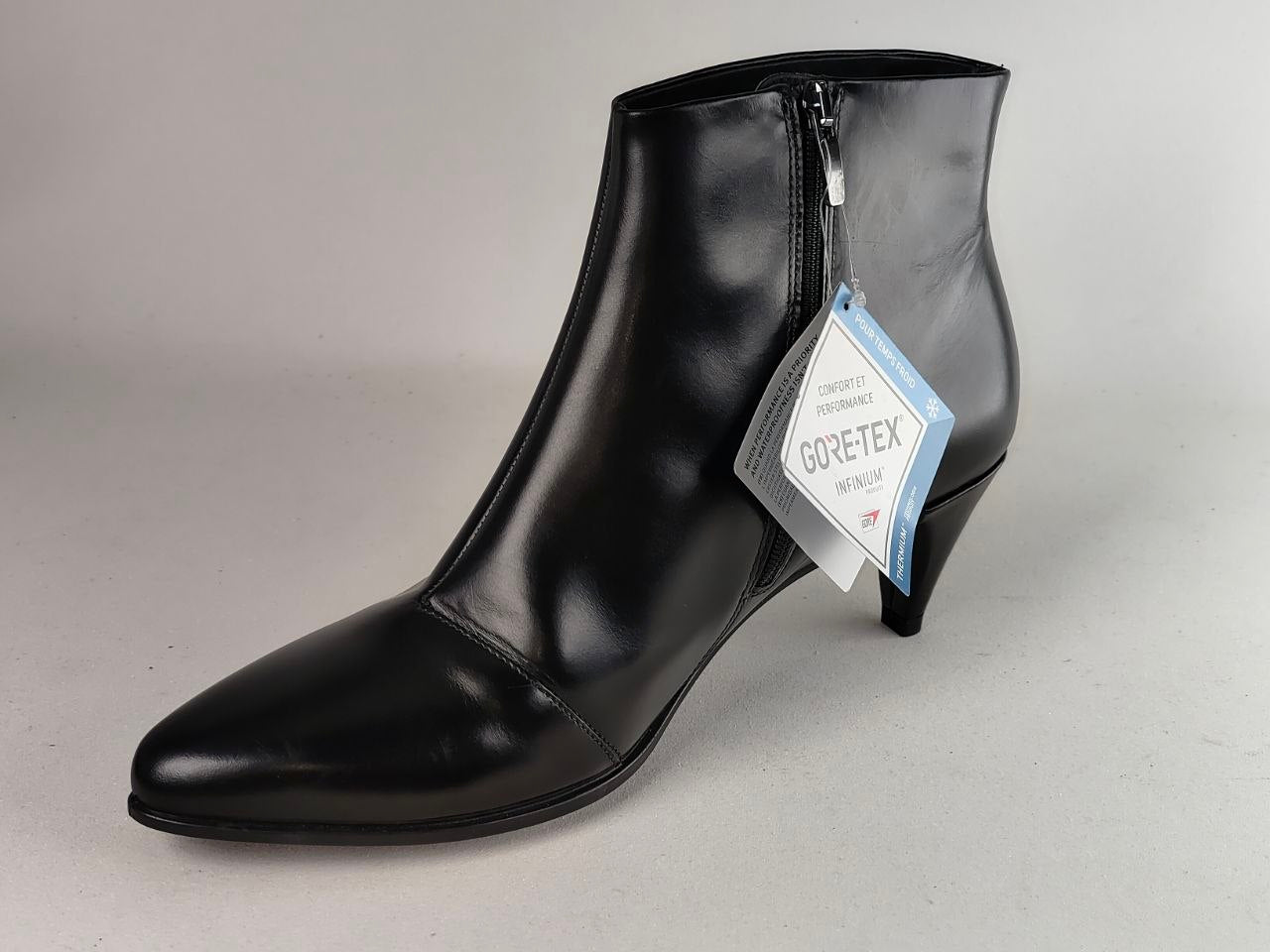 A black leather ankle boot with a pointed toe and a low kitten heel, featuring a side zipper and a hanging GORE-TEX tag, photographed on a neutral light gray background.