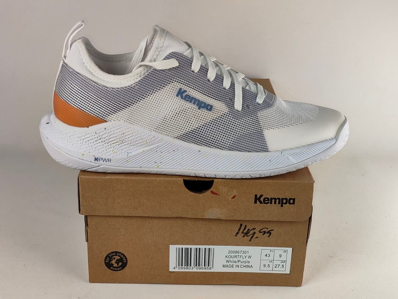 A white, gray, and orange Kempa athletic sneaker resting on top of its brown cardboard shoebox against a plain beige background.