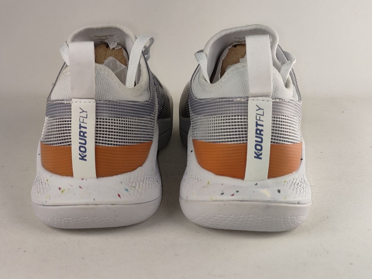 A pair of white Kourtley sneakers shown from the back, featuring gray mesh panels, a vibrant orange accent stripe, and white pull tabs with the brand name 'KOURTFLY' printed vertically.