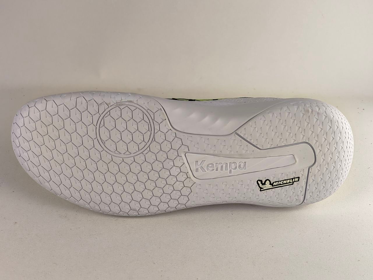 The outsole of a white indoor soccer shoe, showing the textured grip pattern, 'Kempa' branding, and a 'Michelin' tread logo on a light beige background.