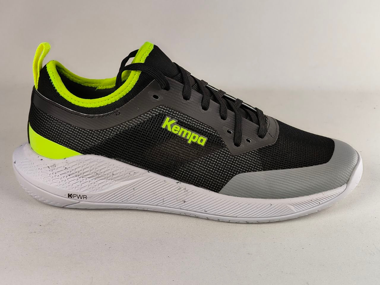 A black and gray running shoe with bright neon yellow-green accents, featuring the 'Kempa' brand logo on the side and a thick white textured midsole.