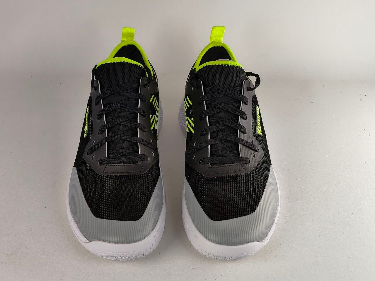 A pair of black and gray athletic sneakers with bright neon yellow accents on the tongue, laces, and side, set against a plain light gray background.