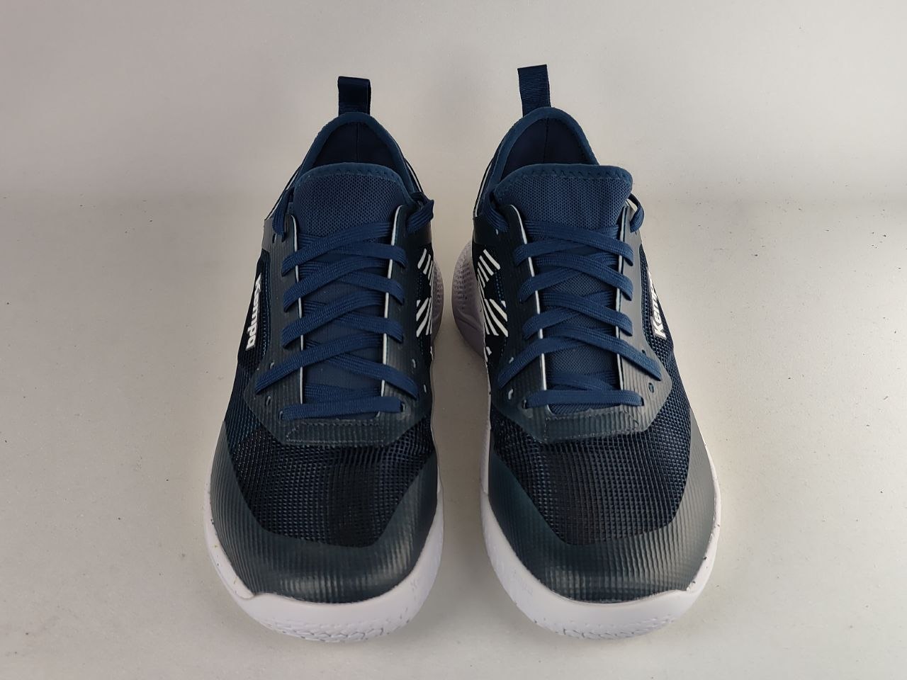 A pair of Nike low-top athletic sneakers in navy blue and dark gray with white soles, shown from the front on a light gray background.