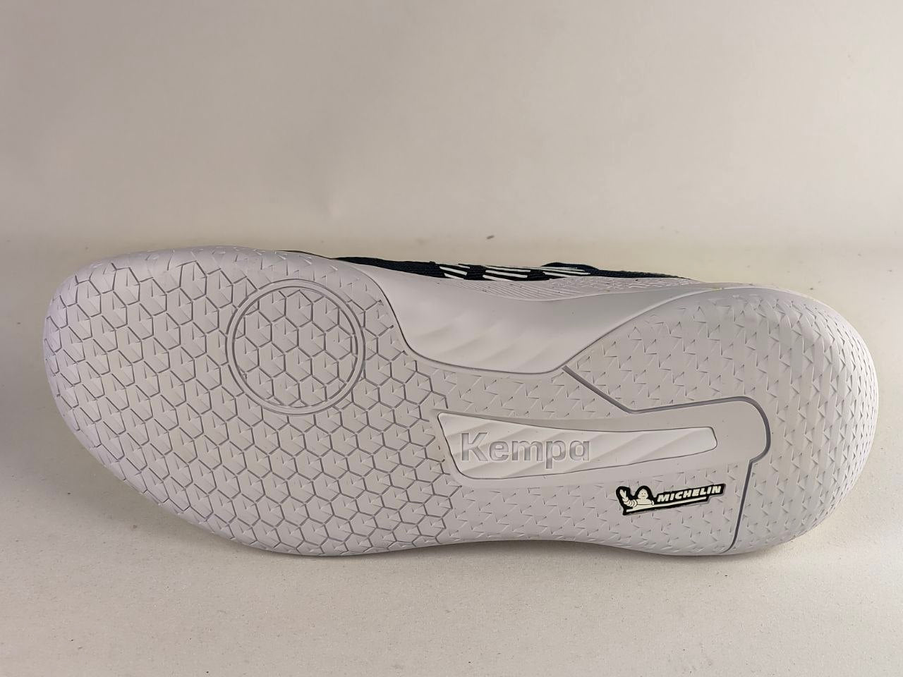 The outsole of a white indoor soccer shoe by Kempa and Michelin, showing a detailed hexagonal tread pattern and brand logos.