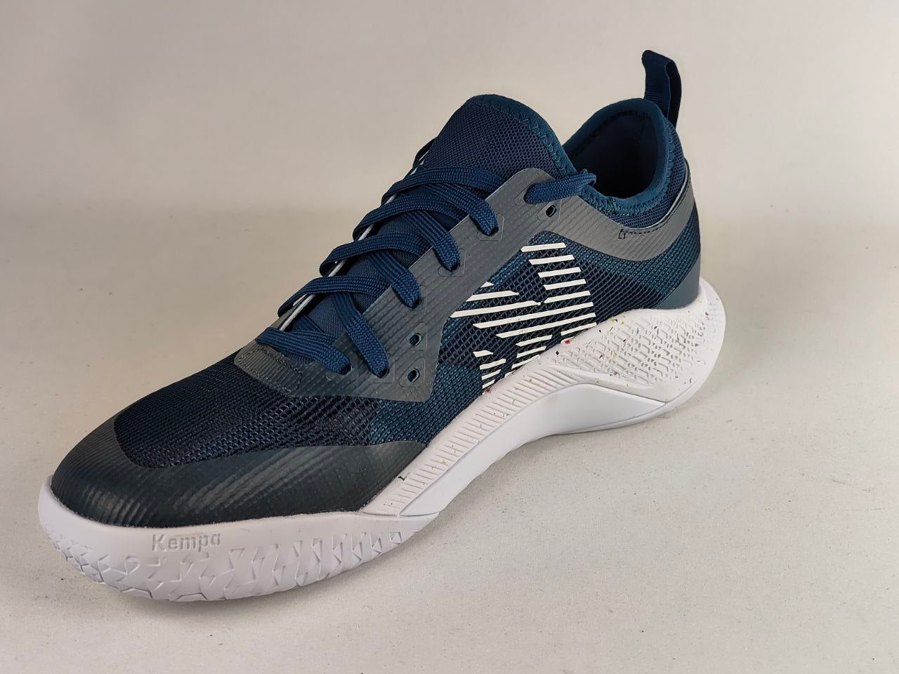 A Kappa athletic sneaker in navy blue and gray with a white textured sole, shown from a three-quarters angle against a neutral light gray background.