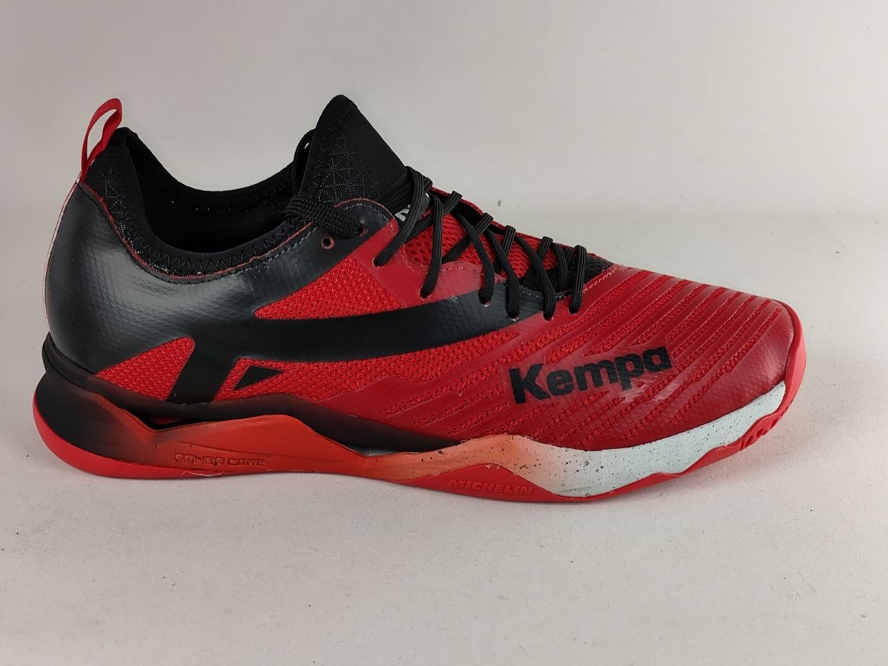 A red and black Kempa athletic shoe shown from the side against a light gray background.
