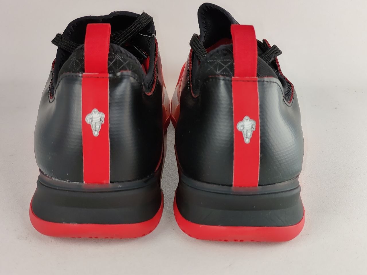 Black and red basketball shoes shown from the back, featuring a vertical red stripe with a silver cross emblem and a red pull tab.