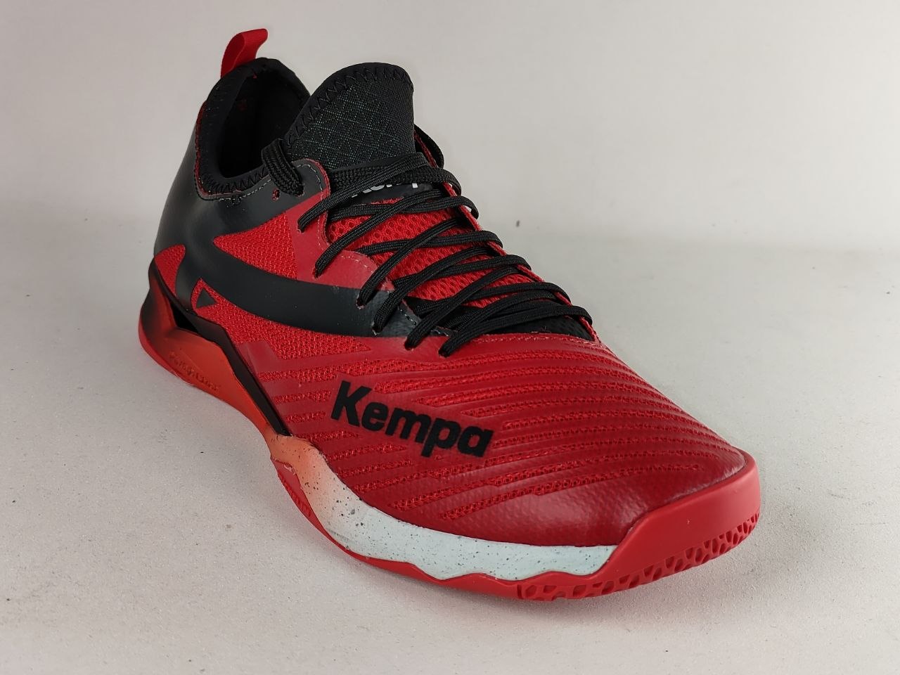 A red and black Kempa indoor court shoe shown from a three-quarters angle against a light gray background.
