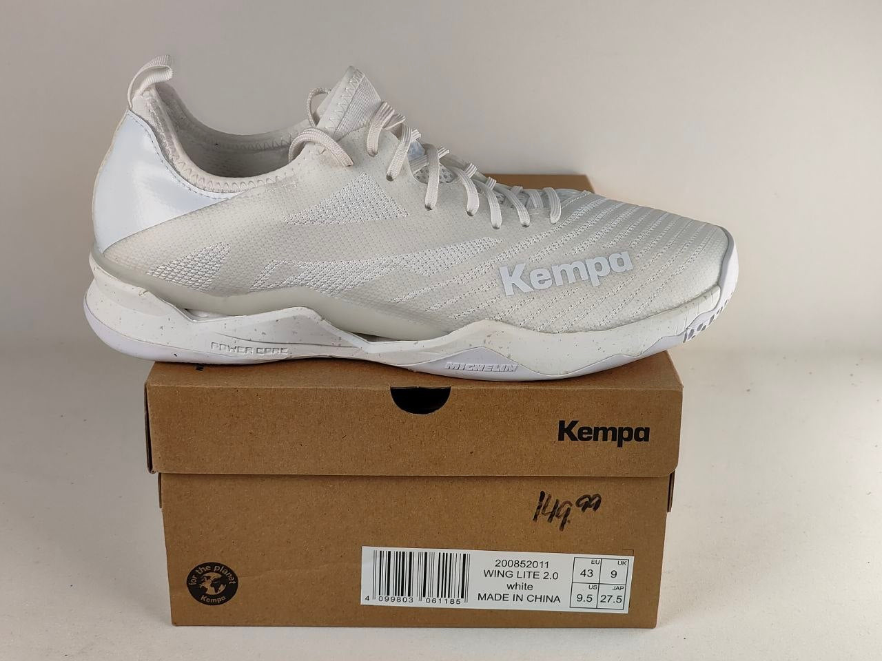 A white Kempa athletic shoe resting on top of its brown cardboard box, photographed against a plain light beige background.
