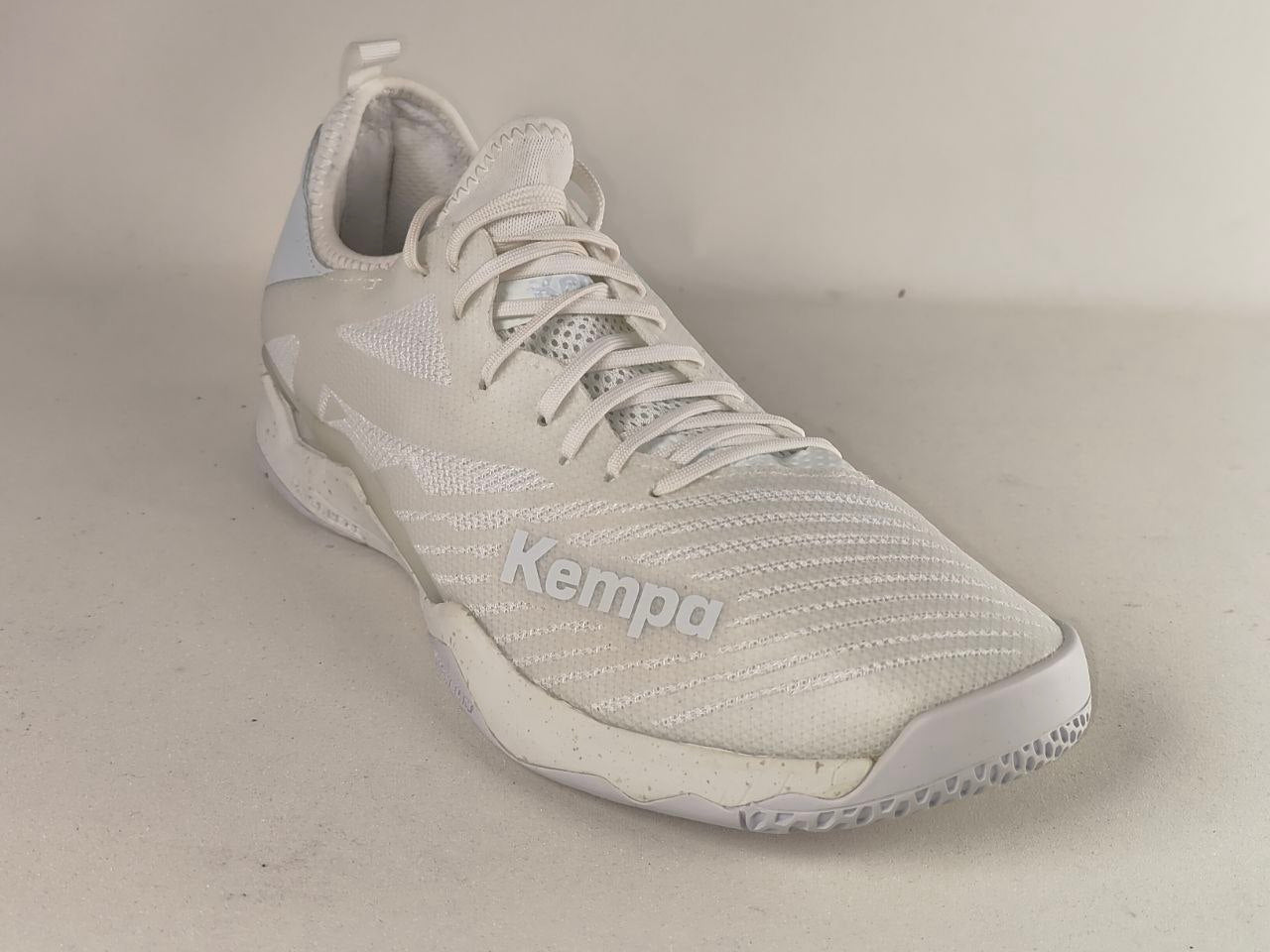 A white and light gray Kempa athletic shoe with a textured mesh upper, white laces, and a white sole, photographed on a neutral beige background.