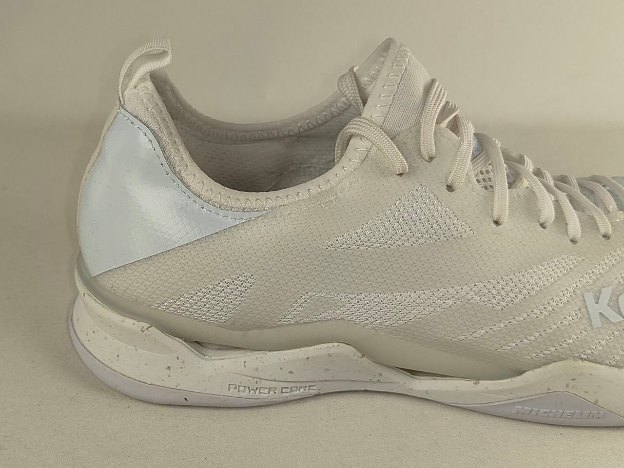 A close-up side view of a K-Swiss athletic shoe in off-white and light gray, showing the textured knit upper, white laces, and midsole with 'POWER CORE' text.