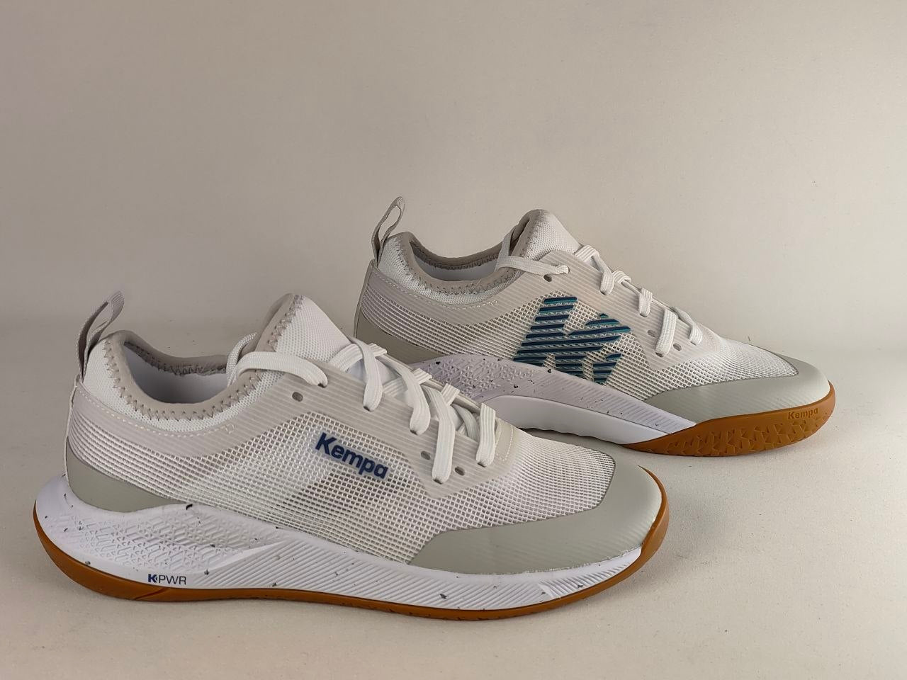 A pair of Kenzo athletic sneakers in white and light gray with a textured blue 'K' logo and a brown gum sole, displayed on a neutral beige background.