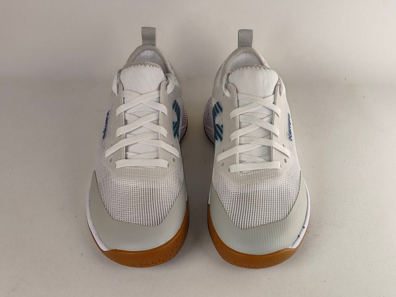 A pair of white athletic sneakers with white laces, light gray accents, and gum brown soles, photographed from the front on a light gray background.
