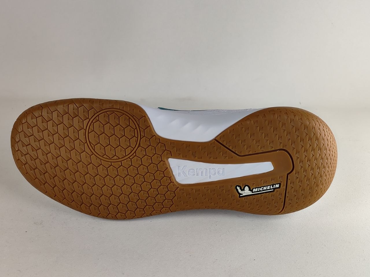 The outsole of a Kempa indoor soccer shoe, showing a brown honeycomb tread pattern, a white heel insert, and a black and white Michelin logo on a light gray background.