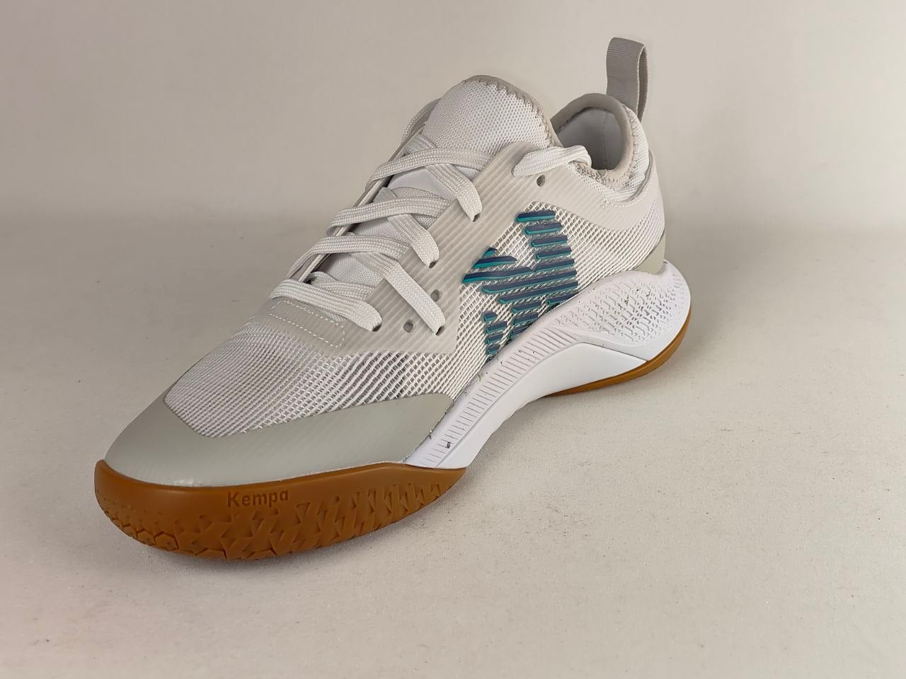 A single Kenda brand athletic shoe in white and light gray with a textured blue side logo and a brown outsole, photographed on a neutral light beige background.