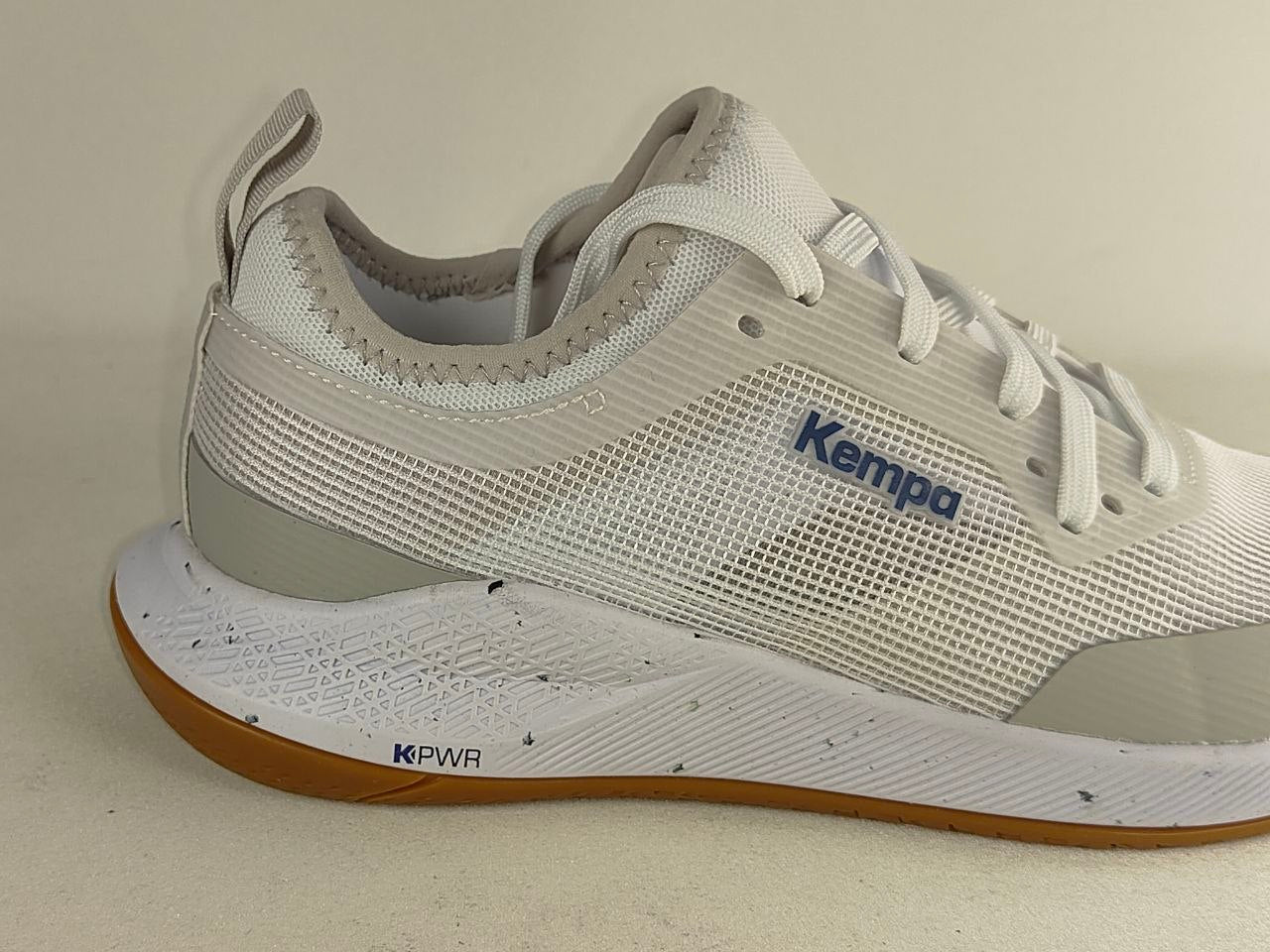 A white and light gray Kempa running shoe with a brown outsole, shown from a side profile view against a neutral beige background.