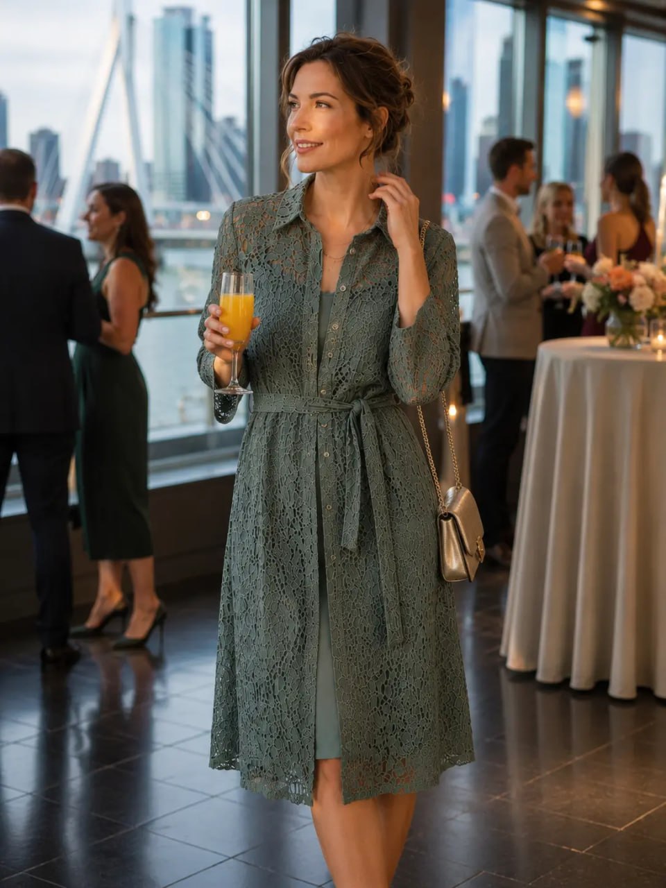 Woman in a green dress holding a glass of orange juice in an indoor setting with people and tables.