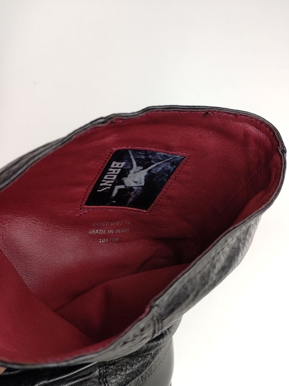 Close-up of the interior of a black leather boot or shoe, showing a deep red lining and a visible black-and-white Brumy brand label.