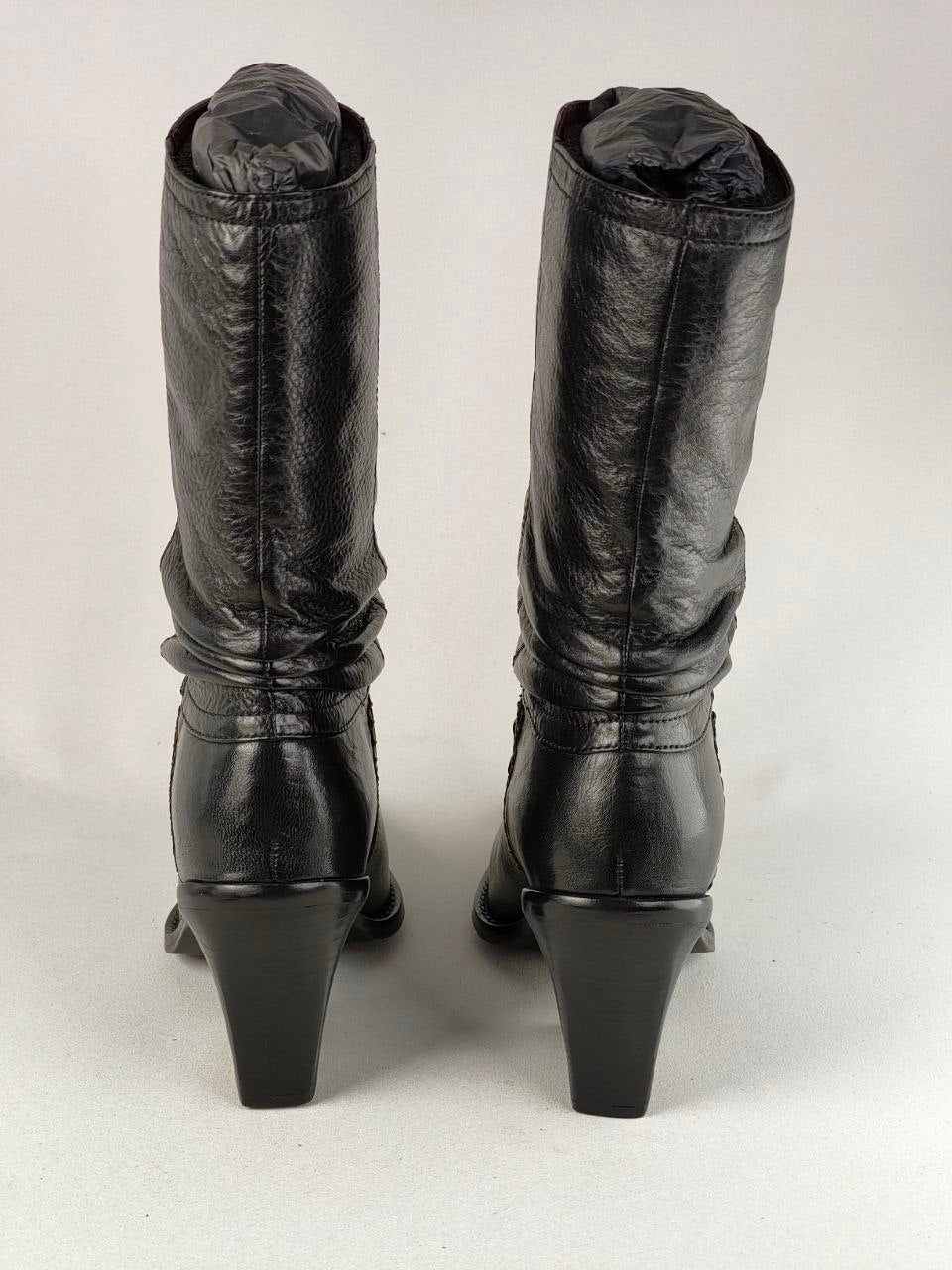A pair of black leather mid-calf boots with a slouchy, gathered upper and a block heel, shown from the back against a light gray background.