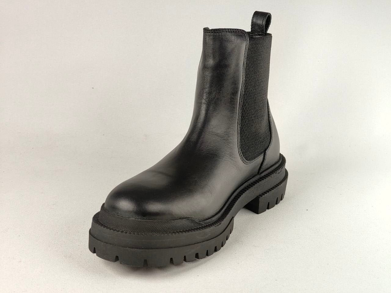A single black leather Chelsea boot with a chunky lug sole, photographed on a light gray studio background.