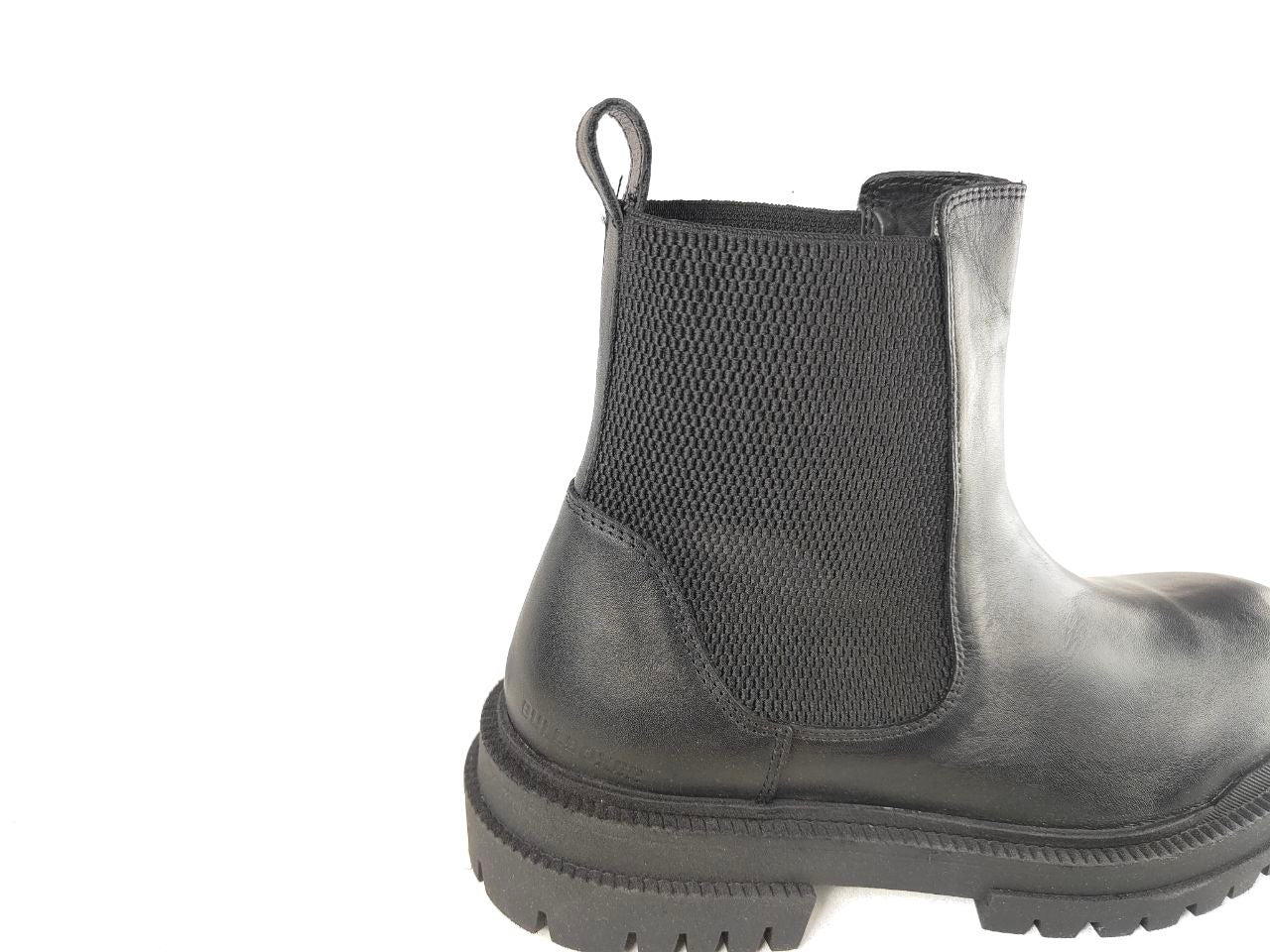 A black leather Chelsea boot with black elastic side panels and a thick lug sole, shown from a side profile on a white background.