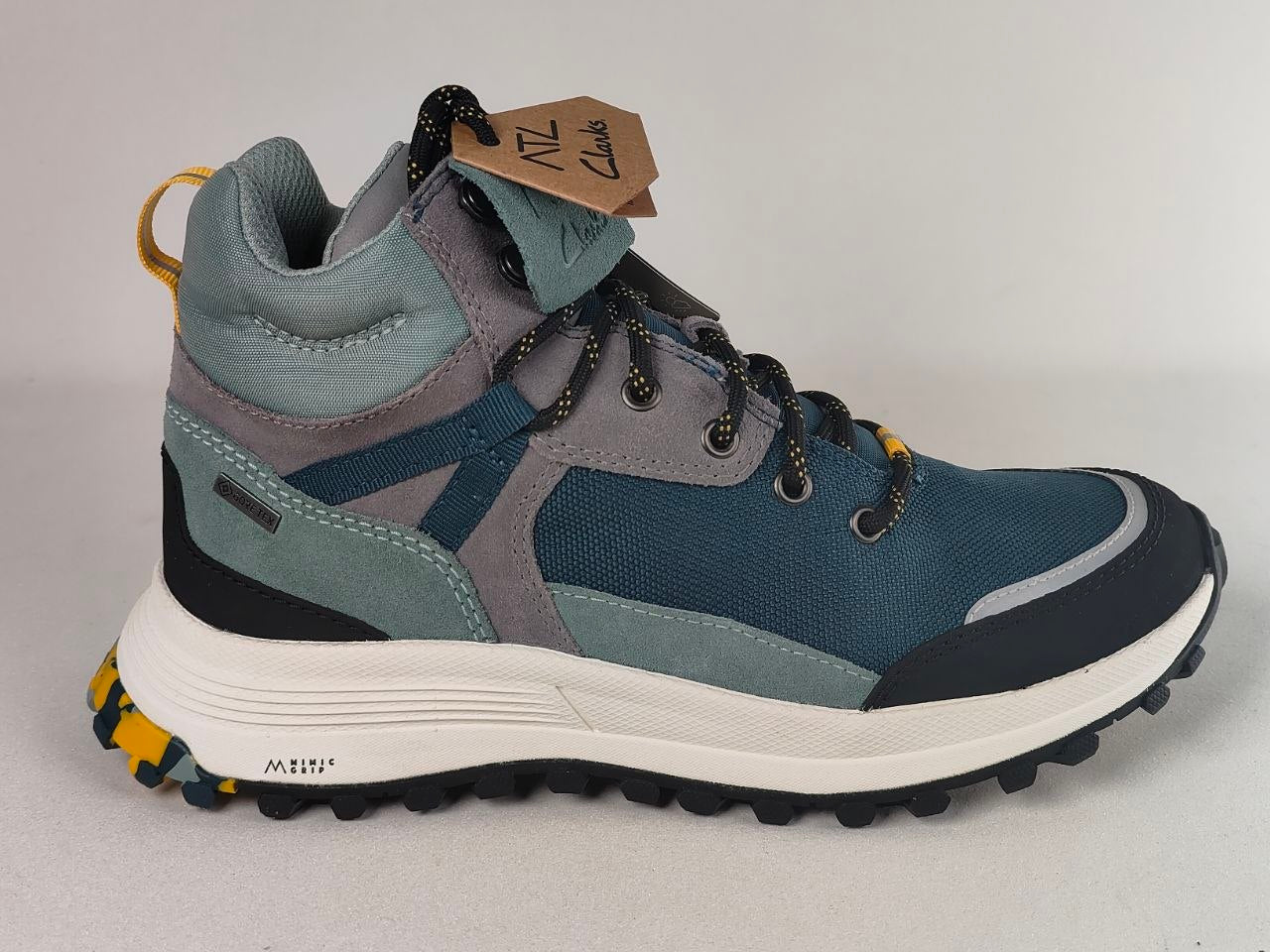 A mid-top hiking boot from Mizz Tread, featuring a blue and gray suede and mesh upper, a white midsole, and a black and yellow lugged outsole, shown against a neutral gray background.