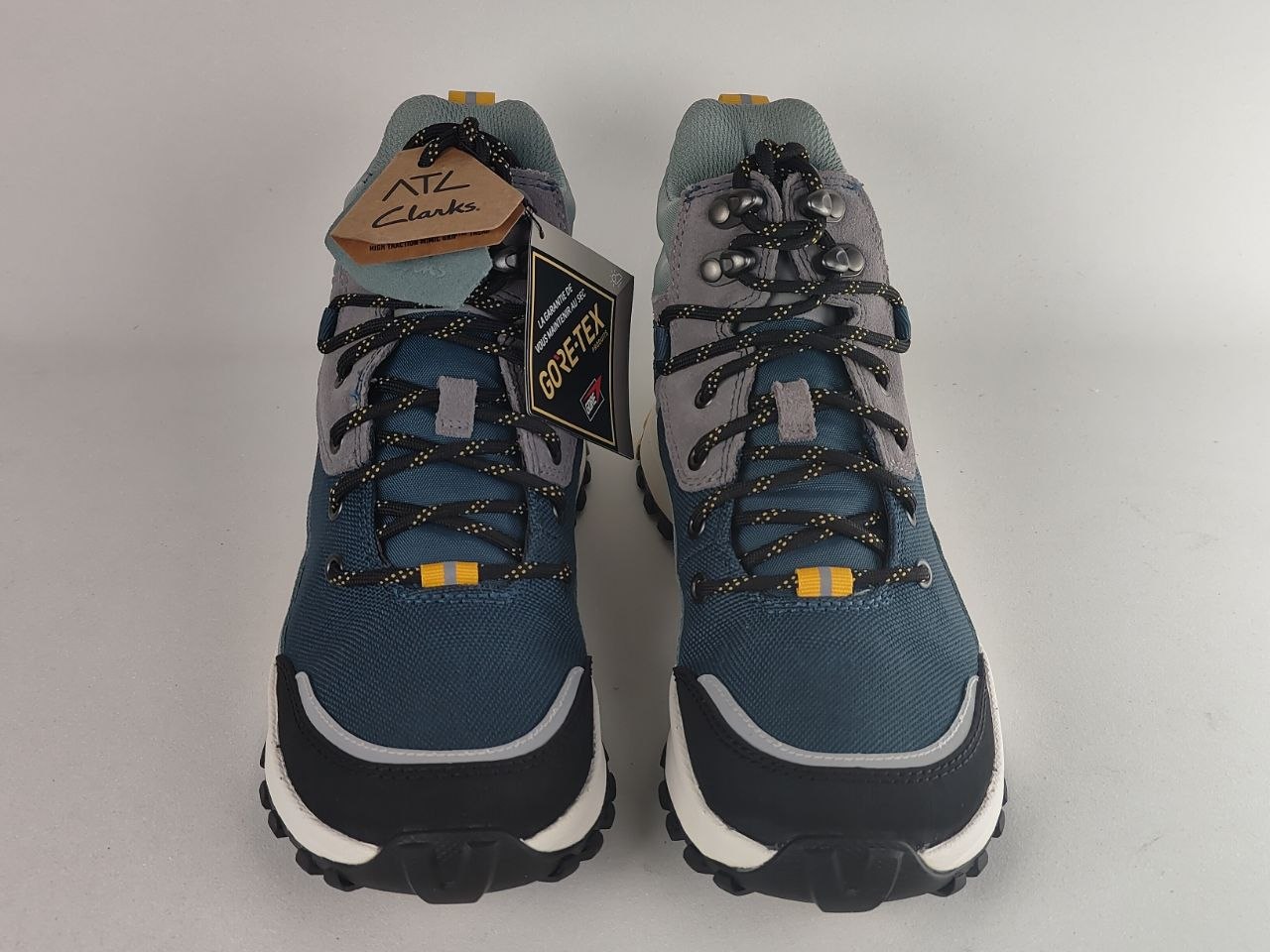 A pair of blue and gray ATG Clarks hiking boots with black and gray laces, featuring a brown leather brand tag and a black GORE-TEX tag, photographed on a light gray background.