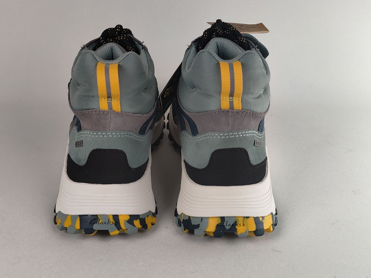 A pair of K-Swiss mid-top sneakers shown from the back, featuring a slate blue-gray upper with yellow stripes, a white midsole, and a yellow and blue patterned outsole.