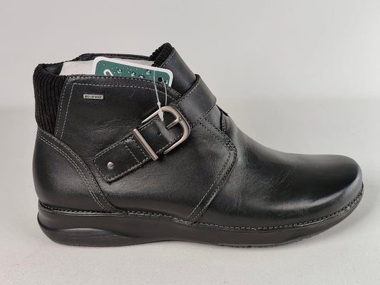 A black leather ankle boot with a buckle strap closure, black ribbed knit collar, and a low wedge heel, shown against a light gray background.