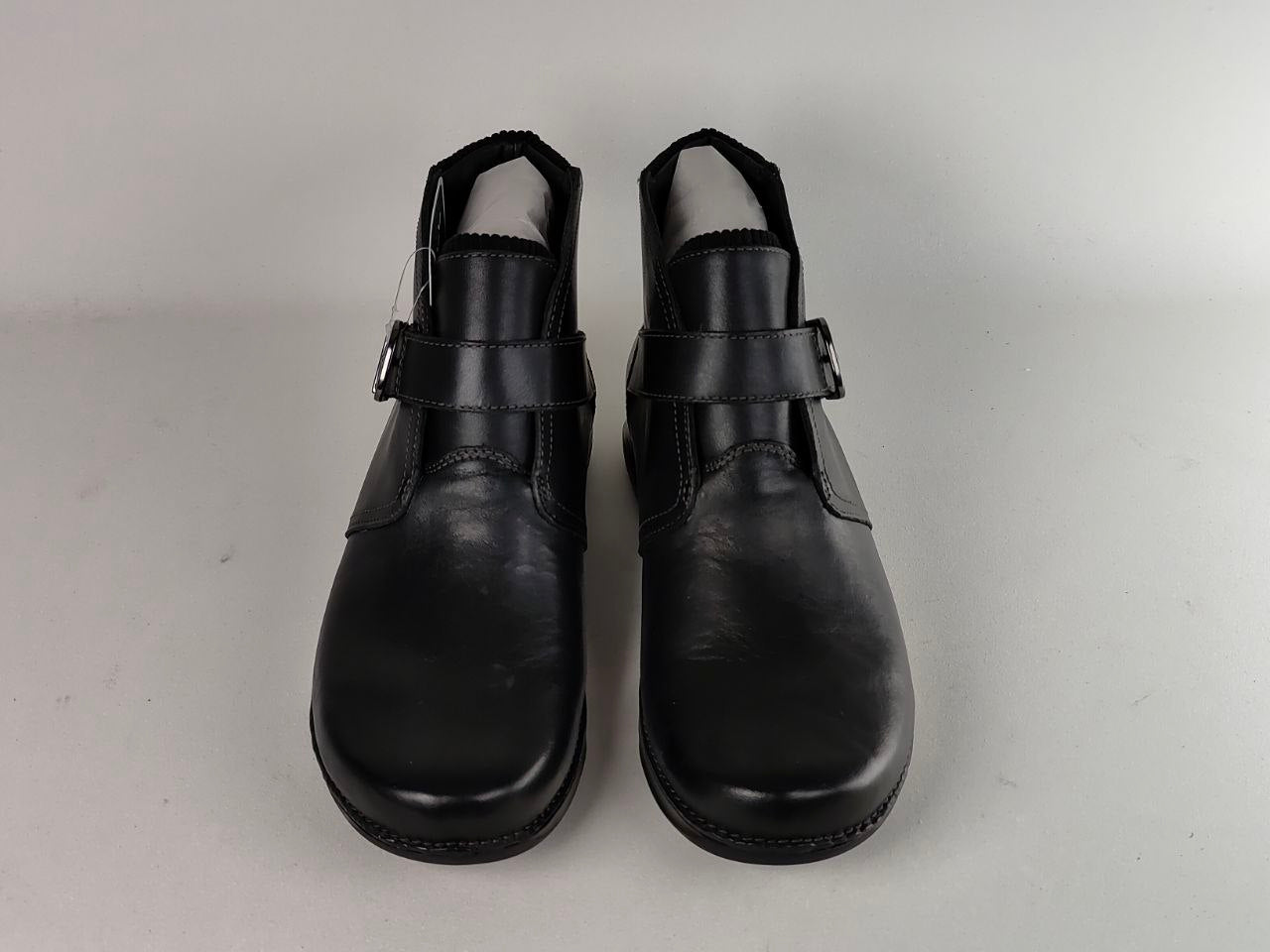A pair of black leather ankle boots with buckle straps, shown from the front on a light gray background.