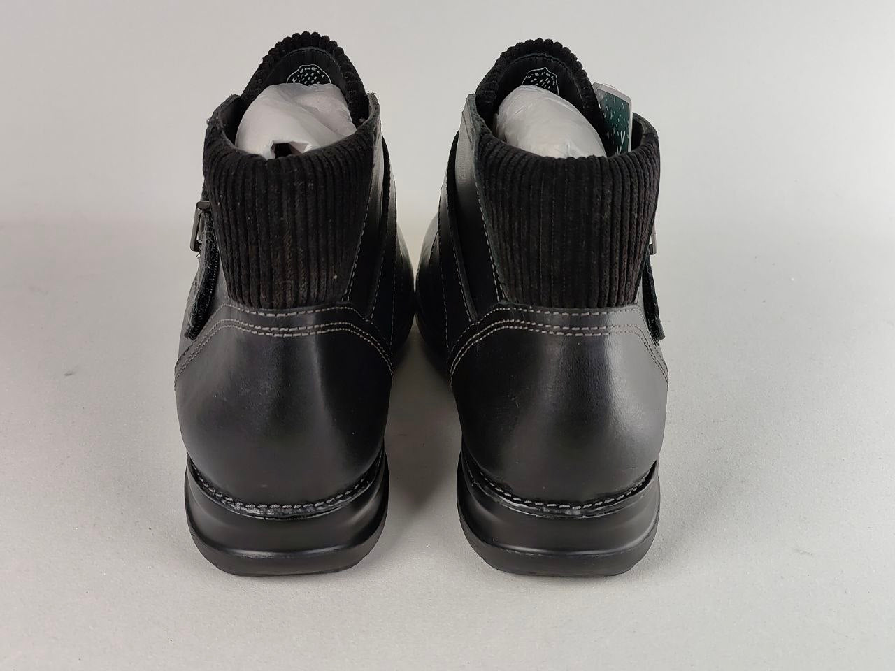 A pair of black leather ankle boots with black ribbed knit cuffs, shown from the back on a light gray background.