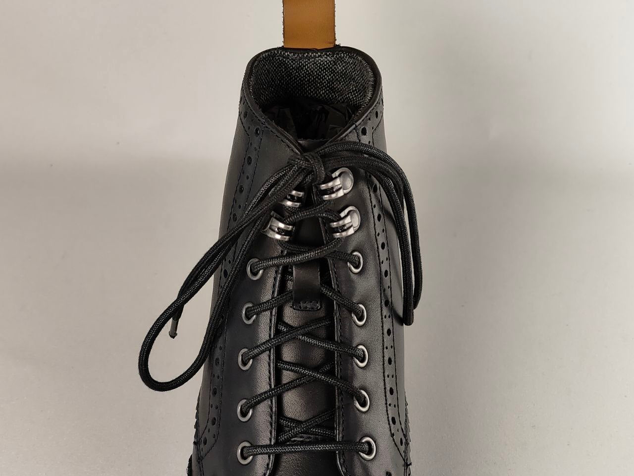 Black leather boot with laces on a neutral background