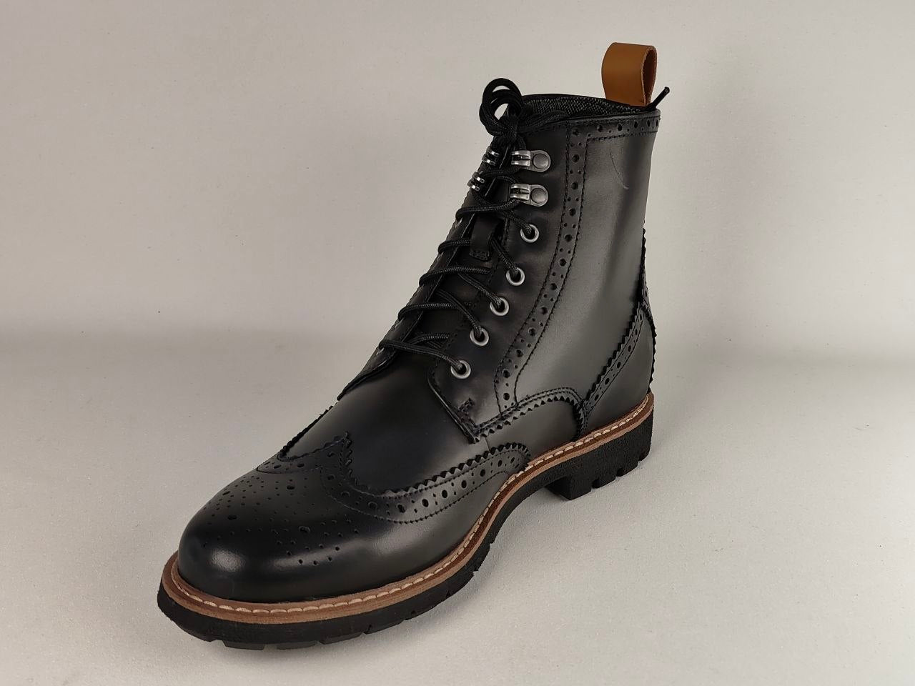 Black leather boot with brown sole on a light gray background