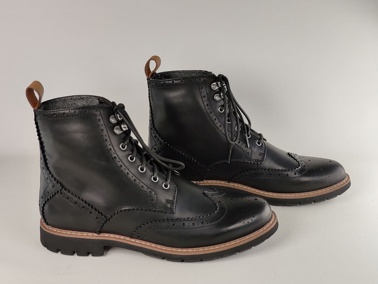 Pair of black leather boots with brown soles on a light gray background
