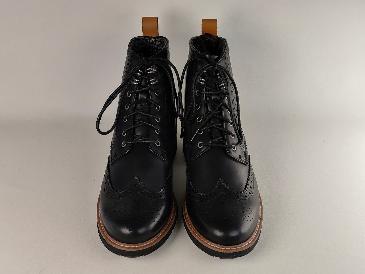 Pair of black leather boots with brown soles on a light gray background